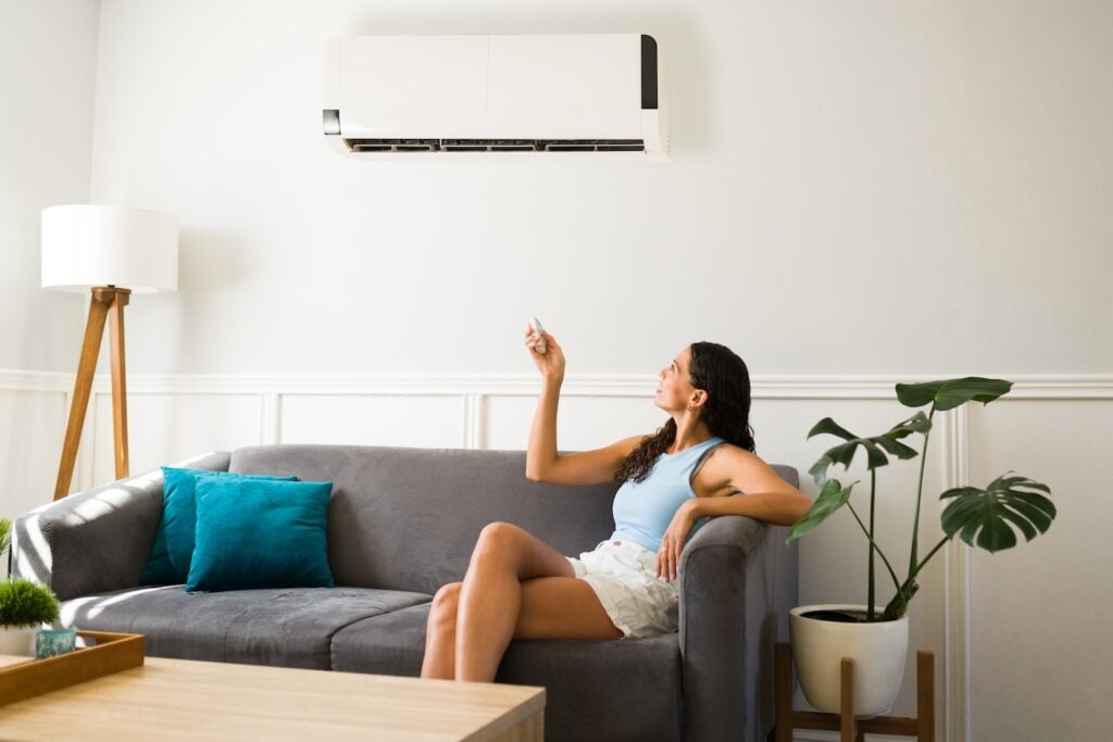 Relaxed young woman sitting on the couch and using the remote to change the room temperature of the ac unit