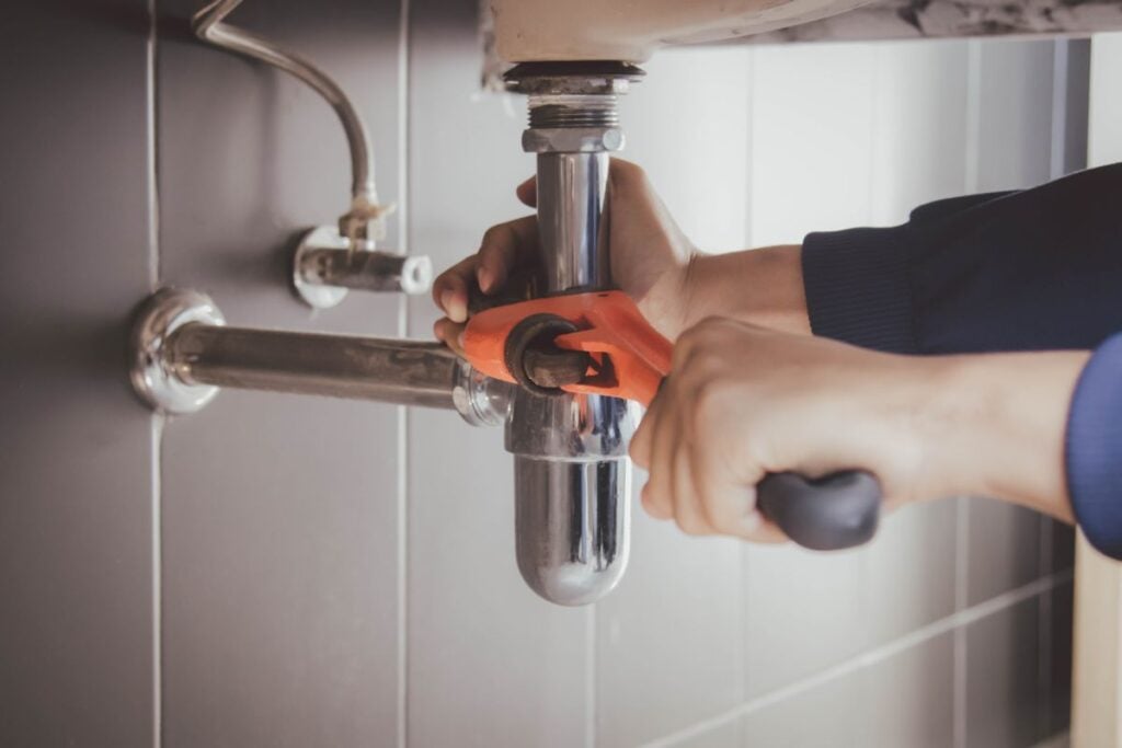 kitchen sink plumbing hand using wrench to adjust pipe