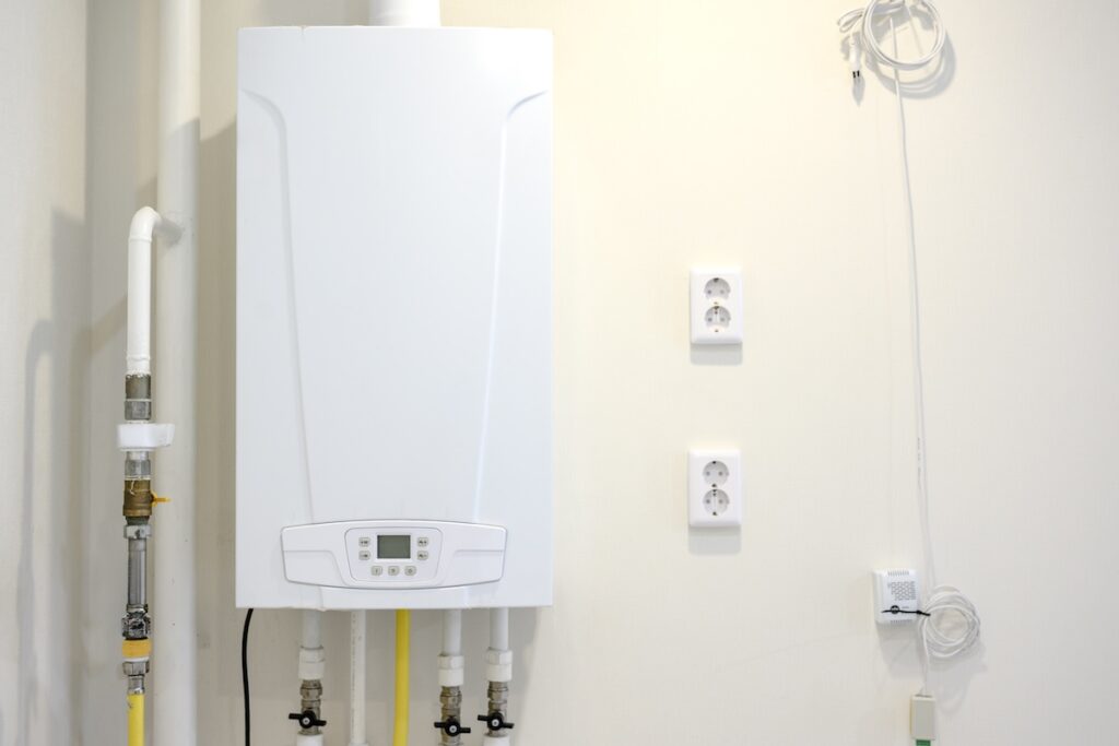Tankless water heater installed on a wall, featuring visible pipes and electrical outlets, in a clean and modern interior setting