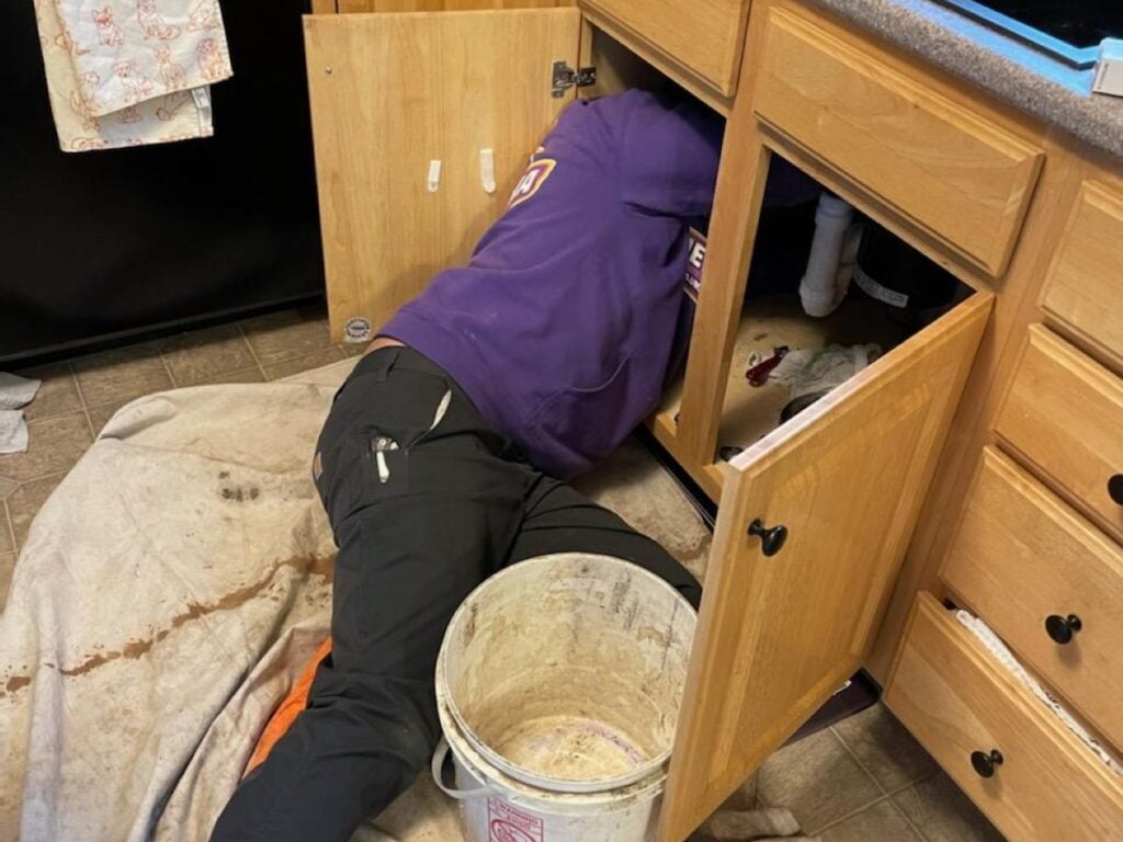 clogged drain worker laying on the floor fixing sink
